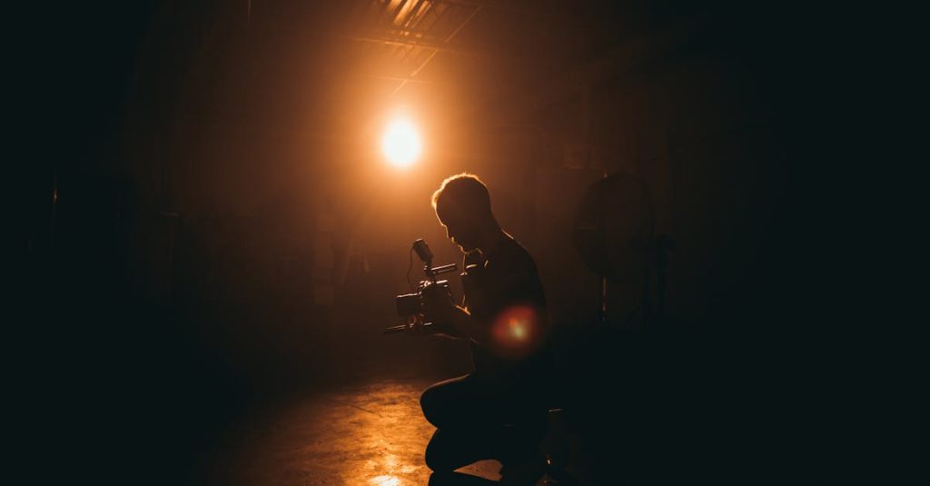 Silhouette of a cinematographer operating a camera in a dimly lit studio with dramatic lighting.