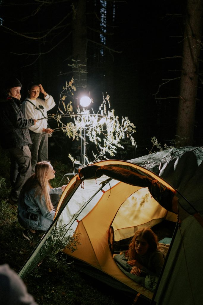 A group of people enjoying a nighttime camping experience, illuminated by a light setup.