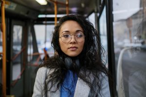 Young woman with eyeglasses and headphones on a bus, showcasing a relaxed commute.