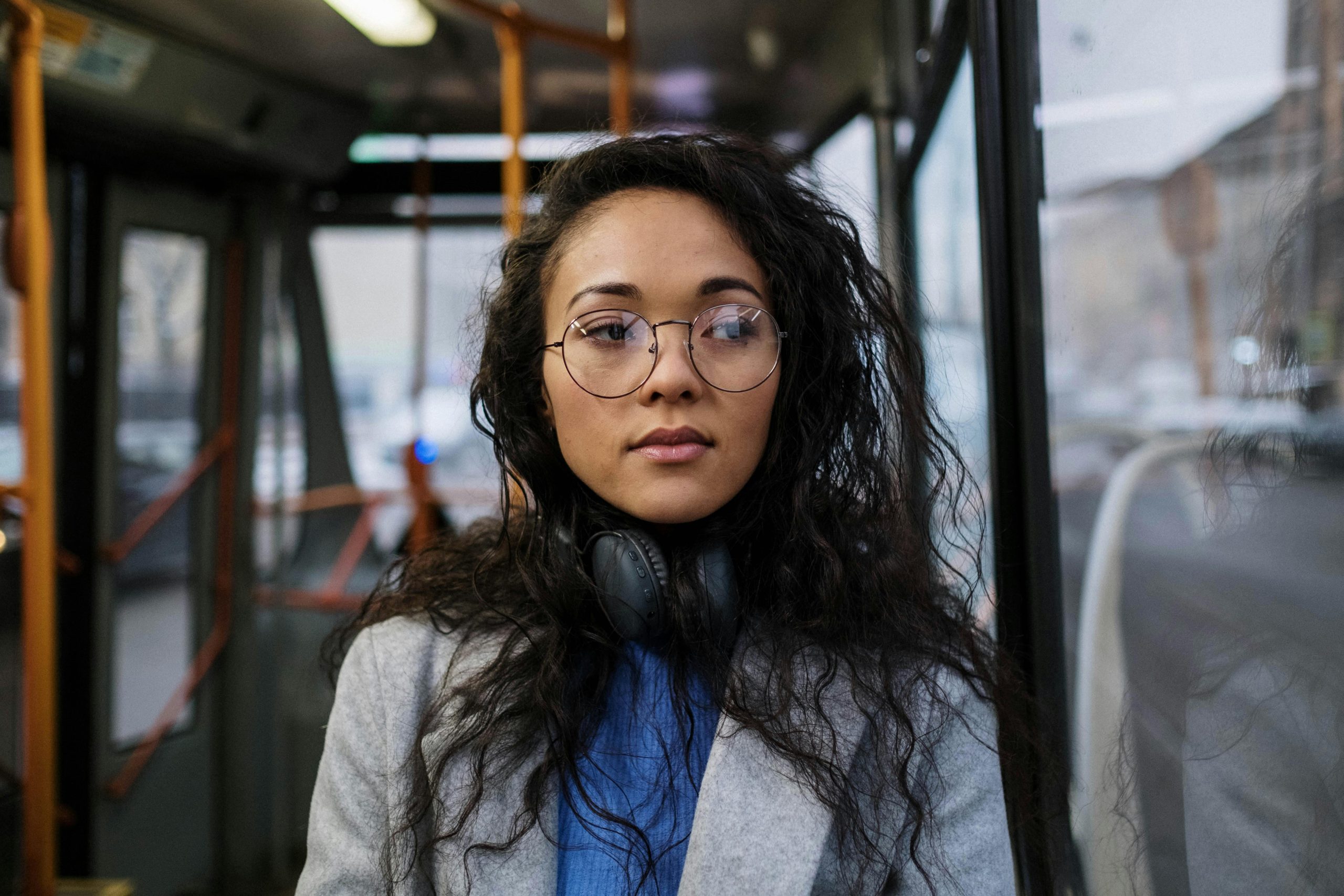 Young woman with eyeglasses and headphones on a bus, showcasing a relaxed commute.